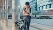 © tirachard - Smile asian businesswoman with backpack use smart phone look camera in city stand at street with bike go to work at office. Sport girl use phone for work. Commute to work, Business commuter in city.