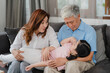 © tirachard - Asian grandparents talking with granddaughter at home. Senior Chinese, old generation, grandfather and grandmother using family time relax with young girl kid lying on sofa in living room concept.