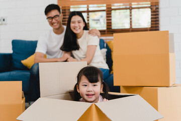 Happy Asian young family homeowners bought new house. Korean Mom, Dad, and daughter playing together during unpacking in new home after moving in relocation sitting on floor with boxes together.