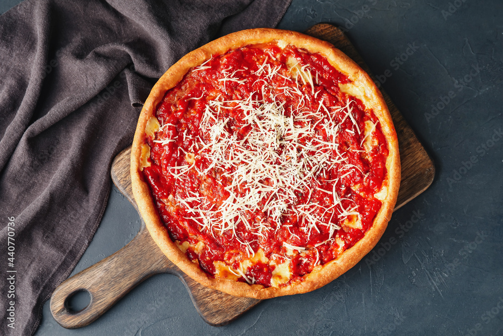Board with tasty Chicago-style pizza on dark background