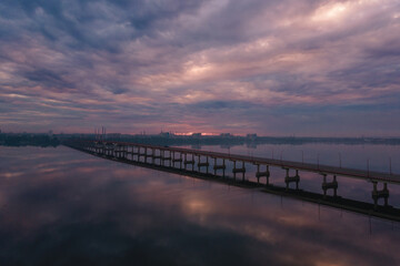 Aerial drone filmed sunset, burning sky over the city and water, beautiful sunset or sunrise. Panoramic view over the bridge with the sun