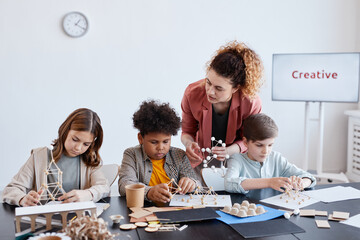 Wall Mural - Group of three children making wooden models during art and craft class in school with female teacher