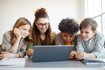 Wall Mural - Portrait of smiling female teacher using computer with diverse group of children