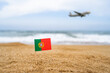 © flowertiare - Flag of Portugal in the form of a toothpick in the sand of beach opposite sea wave with landing airplane. Travel concept
