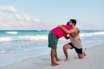 homosexual couple of two men, making a marriage proposal on the coast of cancun beach in the mayan rivera maya mexico, with a turquoise sea in the background.