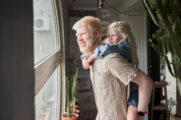 Wall Mural - Girl embracing with her albino father and looking at the window with interest