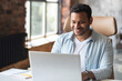 © Vadim Pastuh - Intelligent indian businessman using a laptop in the office. Smart smiling man entrepreneur looks through emails, analyzes tasks, checks report. Hispanic freelancer in modern loft office