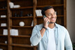 © Vadim Pastuh - Smiling and positive indian guy in casual shirt talking by the smartphone in the modern office. Cheerful mixed-race man has phone conversation. Joyful male employee speaking on mobile phone indoors