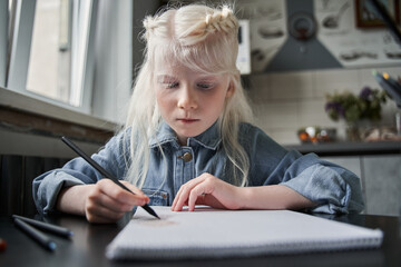 Wall Mural - Girl sitting and drawing her picture with calmness at the table at the kitchen