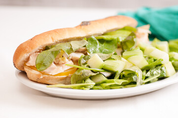 Wall Mural - Closeup shot of cucumber salad with a chicken submarine-style sandwich  on a white background