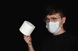 © dg550 - A man wearing a mask and glasses holds toilet paper. Solid black background. Toilet and toilet. Hygiene and sanitation.