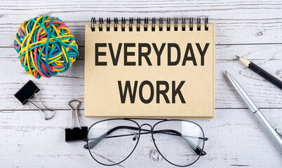 Poster - Notebook with text EVERYDAY WORK and office supplies. View from above. Closeup on white background