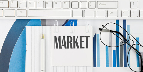 Office desk table with keyboard, chart,glasses and pen. Top view with text MARKET