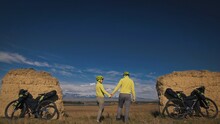 The Man And Woman Travel On Mixed Terrain Cycle Bike Touring With Bikepacking. The Two People Journey With Bicycle Bags. Sport Sportswear In Green Black Colors. Mountain Snow Capped, Stone Arch.