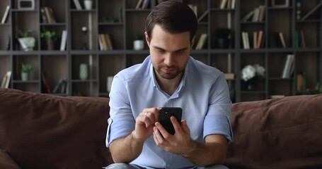 Young handsome single man sit on sofa with smartphone, write message use messenger, e-date services, social media network satisfied user. Modern tech, internet connection everyday usage, fun concept