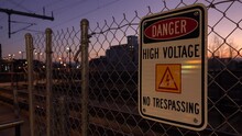 Danger High Voltage No Trespassing Sign On Fence Near Train Tracks At Twilight 4K