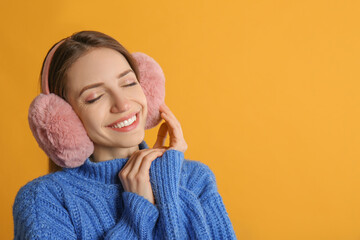 Sticker - Happy woman wearing warm earmuffs on yellow background, space for text