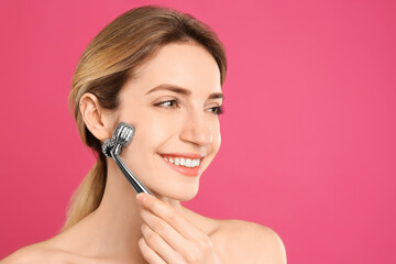 Poster - Young woman using metal face roller on pink background