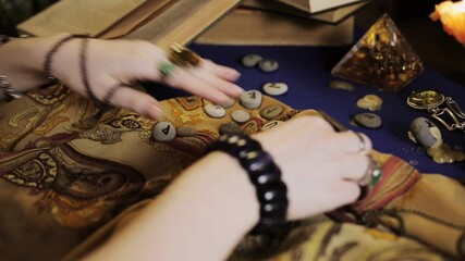 Sticker - Astrology and esotericism. A female fortune teller makes a layout with Runestones, using a book. Hands in rings and bracelets close-up.