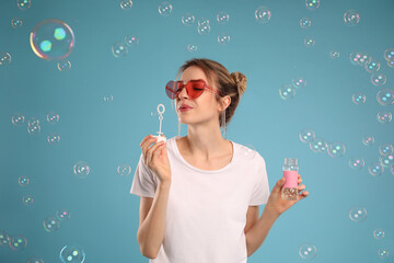 Sticker - Young woman blowing soap bubbles on light blue background