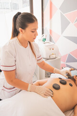 Poster - Vertical shot of a female therapist applying hot stone massage therapy on a woman in the spa