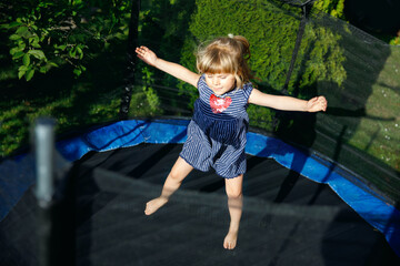 Wall Mural - Little preschool girl jumping on trampoline. Happy funny toddler child having fun with outdoor activity in summer. Sports and exercises for children.