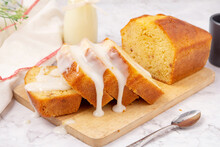 Sliced Pound Cake Topped With Lemon Glaze On A Cutting Board And Spoon Are Marble Table.