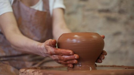 Wall Mural - Sculptor in the studio makes a clay pot close-up. Senior woman is sculpting a bowl behind a rotating potter's wheel