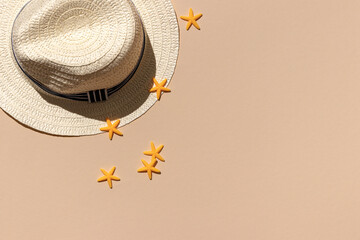 white straw wicker hat on a sand color background with yellow starfishes top view. hard shadows of the sun. minimal concept of travel and vacation with copy space