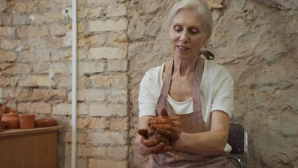 Wall Mural - Senior woman works with clay. Woman potter kneads and moistens the clay before work