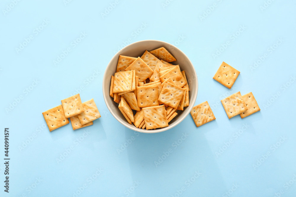 Bowl with tasty crackers on color background