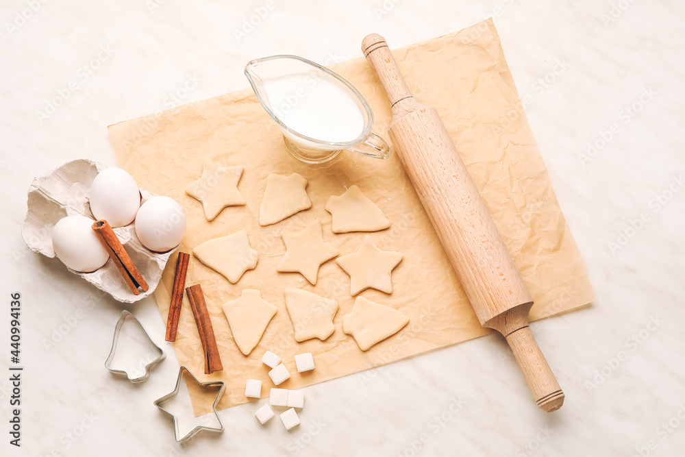 Parchment with uncooked cookies and ingredients on white background
