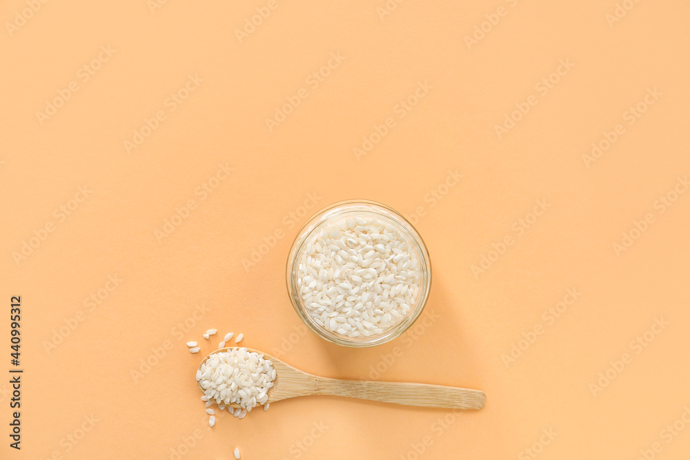 Jar and spoon with raw rice on color background