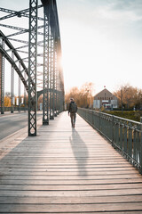 Poster - Young tourist with a backpack walking alone on a wooden bridge during the sunset