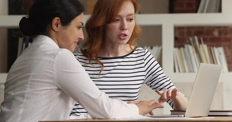 Canvas Print - Happy young indian ethnicity team leader helping concentrated red-haired female colleague with online project on computer. Two mixed race millennial employees developing company growth strategy.