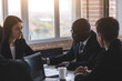 © xartproduction - Mature afroamerican businessman to discuss information with a younger colleague. People working and communicating while sitting at the office desk together with colleagues sitting.