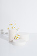 Empty cylindrical podium or plinth with chamomile flowers on a white background. Blank shelf product standing background