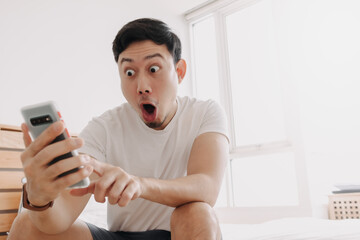 Wow face of Asian man surprised while look at the s'martphone in his apartment.