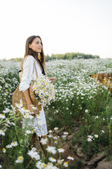 Wall Mural - portrait of a beautiful young Caucasian woman on a chamomile field in a picturesque valley. a young lady in a white cotton dress and a straw hat. holds a bouquet of daisies. 