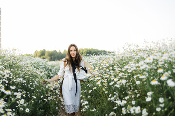 Wall Mural - portrait of a beautiful young Caucasian woman on a chamomile field in a picturesque valley. a young lady in a white cotton dress and a straw hat. holds a bouquet of daisies. 