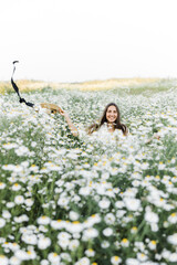 Wall Mural - portrait of a beautiful young Caucasian woman on a chamomile field in a picturesque valley. a young lady in a white dress and a straw hat jumps out of a bush.