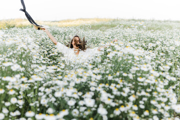 Wall Mural - portrait of a beautiful young Caucasian woman on a chamomile field in a picturesque valley. a young lady in a white dress and a straw hat jumps out of a bush.