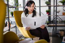 Creative Businesswoman With Headphones Reading Paperwork