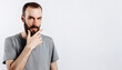 © Daria Lukoiko - Serious puzzled handsome male model with beard holding hand on chin as if thinking about something, squinting at camera with suspicious look and standing over gray background. Man decides what to buy