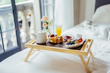 View to the wooden tray with brekfast in the bed in the hotel room with window