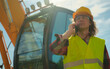 © M-Production - Excavator operator in hard hat talking by smartphone.
