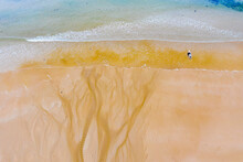 A Solitary Paddle Boarder Entering The Waves Where A Creek Spreads Out And Flows Into The Sea