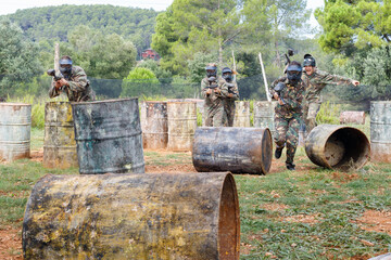 Canvas Print - Team of happy smiling people playing paintball on battlefield outdoor, running with guns