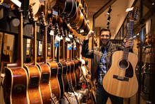 Portrait Of Talented Caucasian Musician In Leather Jacket Who Has Just Purchased Classic Acoustic Guitar In Music Shop.