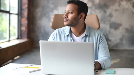 Wall Mural - Optimistic concentrated clever indian freelancer guy using laptop for searching, web surfing, looking away lost in searching ideas for startup, a thoughtful millennial work remotely at home